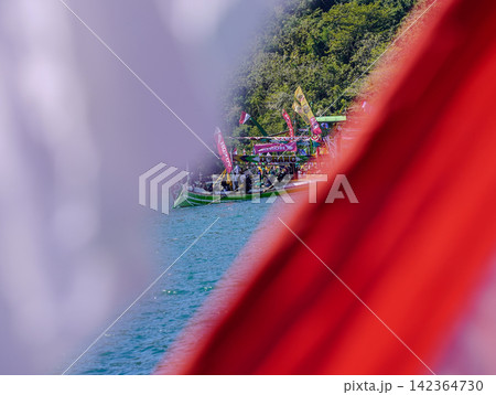 BANYUWANGI, INDONESIA - JULY 1, 2026: A framed view through the Indonesian red and white national flag depicting traditional fishing boats during the Petik Laut sea thanksgiving ceremony in Banyuwangi 142364730