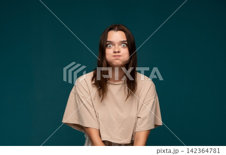 Young woman puffing cheeks, making a funny face, portraying a playful and exaggerated expression Young woman puffing cheeks, making a funny face, portraying a playful and exaggerated expression 142364781