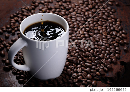 coffee droplets drop on black coffee water in white mug with surrounded by roasted coffee beans on dark red wood table 142366653