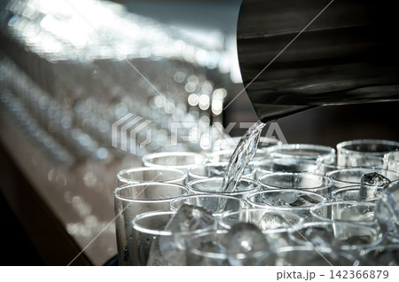 pouring cool pure transparent clear drinking water from the jar to clean glasses on the table 142366879