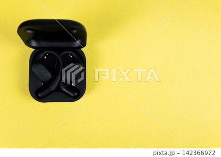 Black wireless headphones with case for mobile phone on the yellow background. Flat lay. Earphones for smartphone. Black wireless headphones with case for mobile phone on the yellow background. Flat lay. Earphones for smartphone. 142366972