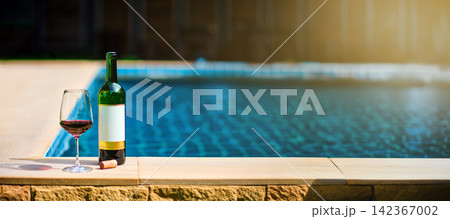 A bottle of red wine and a glass of wine are set on the edge of a clear blue pool, surrounded by a lush green lawn. The afternoon sun shines down, creating a relaxing and inviting atmosphere. A bottle of red wine and a glass of wine are set on the edge of a clear blue pool, surrounded by a lush green lawn. The afternoon sun shines down, creating a relaxing and inviting atmosphere. 142367002