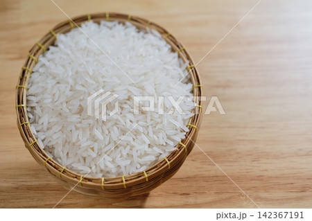 raw Thai's jasmine rice in Thai's traditional style bamboo's bowl on wooden dinner table 142367191