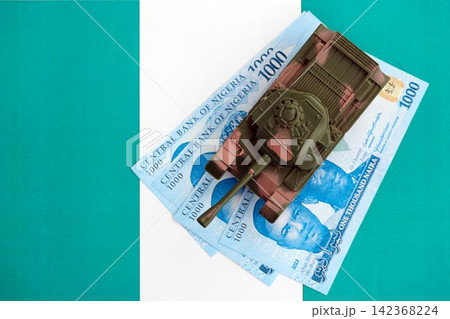 Nigerian naira currency money bills and toy tank on flag. The concept of army funds and weapons sales Nigerian naira currency money bills and toy tank on flag. The concept of army funds and weapons sales 142368224