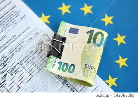 European euro currency money notes bunch on tax form and European union blue flag close up European euro currency money notes bunch on tax form and European union blue flag close up 142368389