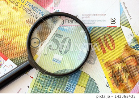 Swiss franc banknotes and magnifying glass. The current francs money bills with loupe lies on table Swiss franc banknotes and magnifying glass. The current francs money bills with loupe lies on table 142368435