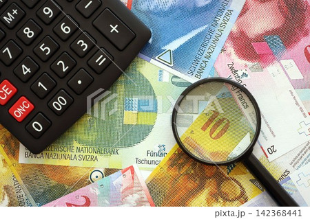 Swiss franc banknotes and calculator with magnifying glass. The current francs money bills and calc 142368441