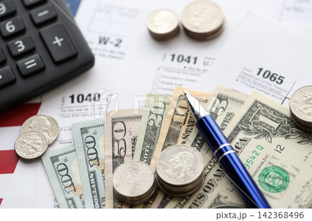American US dollars money bills and coins with pen and calculator on IRS tax form blanks American US dollars money bills and coins with pen and calculator on IRS tax form blanks 142368496