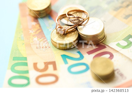 European union Euro money bills and coins with wedding rings on blue table European union Euro money bills and coins with wedding rings on blue table 142368513