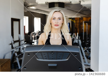 Determined sportswoman running on treadmill in modern gym Determined sportswoman running on treadmill in modern gym 142368880