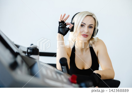 Fit woman listening music and gesturing ok sign while using treadmill Fit woman listening music and gesturing ok sign while using treadmill 142368889