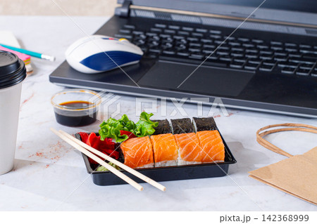 Sushi lunch on a desk with a laptop and coffee cup during work hours,no people Sushi lunch on a desk with a laptop and coffee cup during work hours,no people 142368999