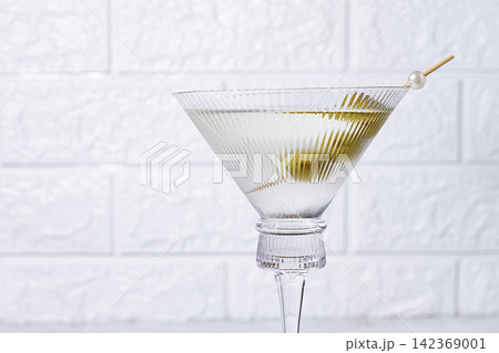 A martini glass, with green olives stands, on a marble surface, in bright light, in a modern environment, no people A martini glass, with green olives stands, on a marble surface, in bright light, in a modern environment, no people 142369001