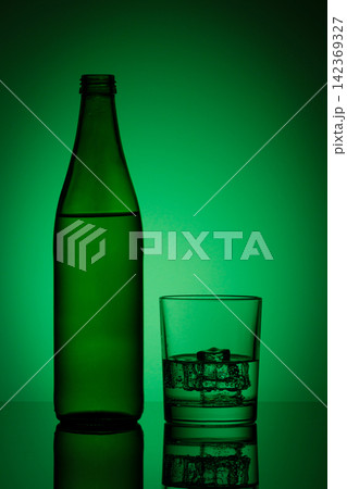 beautiful bottle with water and glass with ice and water on a green background beautiful bottle with water and glass with ice and water on a green background 142369327