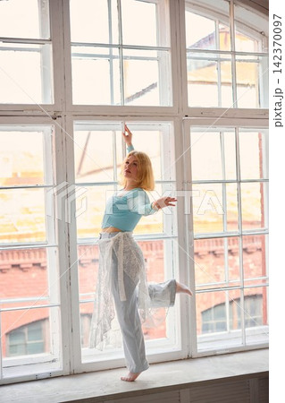 Blonde ballet student skillfully executing arabesque near window Blonde ballet student skillfully executing arabesque near window 142370097