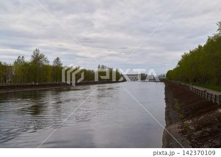Tranquil canal with reflective surface amid greeneries and cloudy sky 142370109