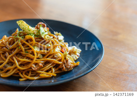 照りのある麺と具材が特徴の焼きそば。ダークな皿に盛り付けられ、食欲をそそる一枚。 142371169