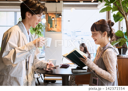 カフェで本を見せながら会話する若い男女のカップル カフェで本を見せながら会話する若い男女のカップル 142371554