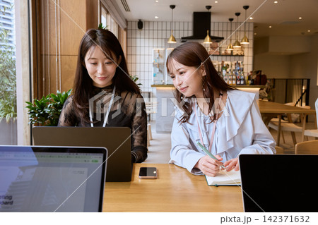 カフェスペースでノートパソコンを見ながら打ち合わせをする二人の若い女性ビジネスパーソン 142371632