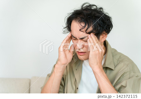 頭痛と体調不良でこめかみを押さえる中年男性 頭痛と体調不良でこめかみを押さえる中年男性 142372115