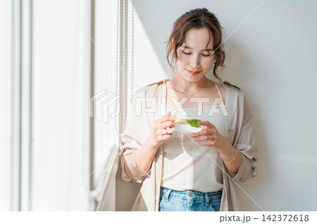 窓辺でハーブティーを楽しみリラックスする女性 窓辺でハーブティーを楽しみリラックスする女性 142372618