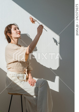 光と影の中でドライフラワーを持つナチュラルファッションの大人の女性 光と影の中でドライフラワーを持つナチュラルファッションの大人の女性 142373075