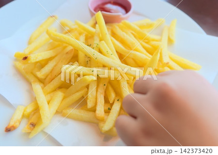 ケチャップを添えた黄金色のフライドポテトに手を伸ばす食事シーン ケチャップを添えた黄金色のフライドポテトに手を伸ばす食事シーン 142373420