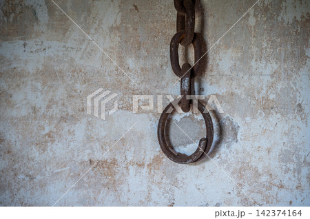 A rusty metal shackle (or handcuff) hanging on the wall. A shackle is a restraint, either physical or psychological, that restricts movement. A rusty metal shackle (or handcuff) hanging on the wall. A shackle is a restraint, either physical or psychological, that restricts movement. 142374164