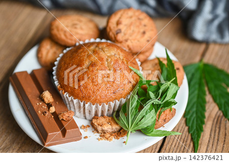 Cannabis food cookies with cake chocolate cannabis leaf marijuana herb on wooden and dark background, delicious sweet dessert cookie with hemp leaf plant THC CBD herbs food snack and medical top view Cannabis food cookies with cake chocolate cannabis leaf marijuana herb on wooden and dark background, delicious sweet dessert cookie with hemp leaf plant THC CBD herbs food snack and medical top view 142376421