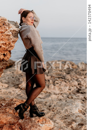Woman coast fashion young lady in sweater and skirt posing on rocky shoreline by the calm ocean with scenic views Woman coast fashion young lady in sweater and skirt posing on rocky shoreline by the calm ocean with scenic views 142378494