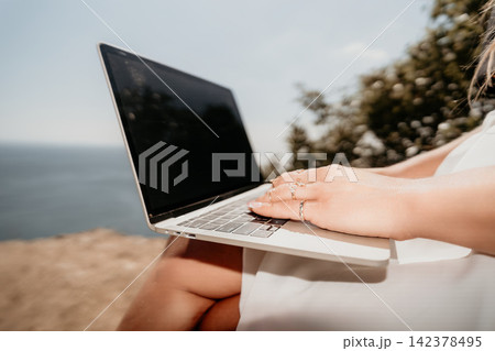 Laptop working freelance woman typing on her silver computer while sitting on a scenic cliff overlooking the ocean during sunny day Laptop working freelance woman typing on her silver computer while sitting on a scenic cliff overlooking the ocean during sunny day 142378495