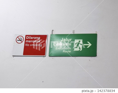 Wall mounted safety signs including red no smoking icon and green evacuation route arrow for emergency building exit. Wall mounted safety signs including red no smoking icon and green evacuation route arrow for emergency building exit. 142378834