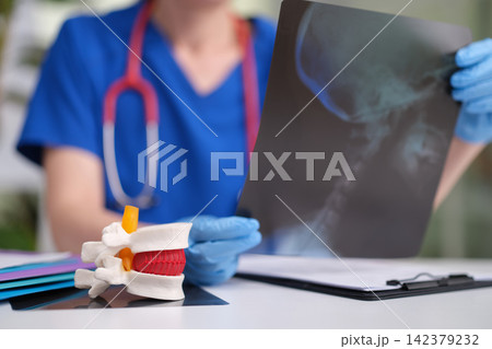 medical professional closely examines spine model in clinical office setting with stethoscope and gloves, focused and detailed close-up view of hands and objects. 142379232
