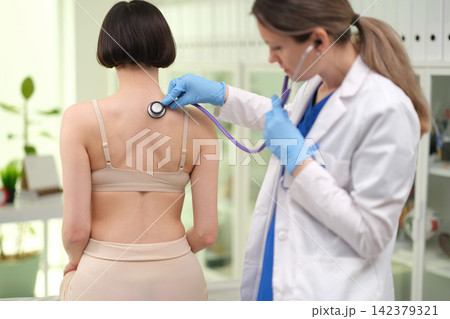 Doctor uses stethoscope to listen to back of patient with pneumonia in clinic Doctor uses stethoscope to listen to back of patient with pneumonia in clinic 142379321