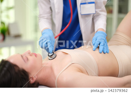 Doctor listens to patient heart and lungs with stethoscopes in clinic closeup 142379362