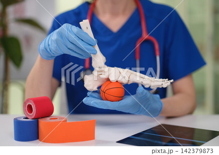 Doctor physical therapist demonstrates to massage foot of artificial human model using ball closeup Doctor physical therapist demonstrates to massage foot of artificial human model using ball closeup 142379873