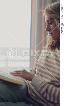 Vertical video. Woman reading book on sofa at home. Calm and comfortable. Vertical video. Woman reading book on sofa at home. Calm and comfortable. 142379893