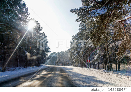 Scenic winter road winding through a snowy pine forest on a bright sunny day with sun rays. Travel, adventure, winter landscape, and seasonal concept Scenic winter road winding through a snowy pine forest on a bright sunny day with sun rays. Travel, adventure, winter landscape, and seasonal concept 142380474