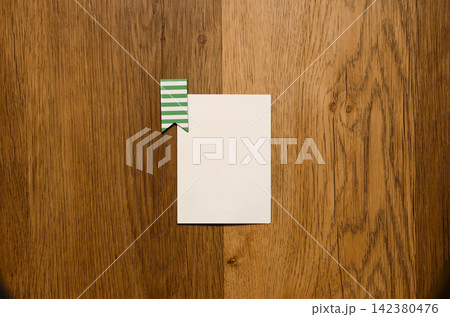 Top-down view of a blank white card with a green striped paper clip on a textured wooden table background. Mockup, design, and note concept Top-down view of a blank white card with a green striped paper clip on a textured wooden table background. Mockup, design, and note concept 142380476