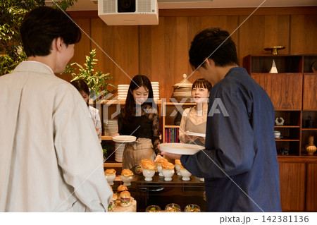 立食パーティーでビュッフェ料理を楽しむ若い男女のグループ 立食パーティーでビュッフェ料理を楽しむ若い男女のグループ 142381136
