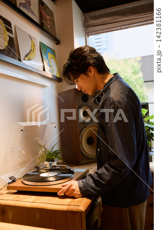 自宅でレコードプレーヤーにレコードをセットする若い男性 142381166