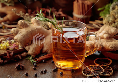 Warming herbal tea with fresh ginger, dried orange slices, juniper berries and spices served in a glass mug. Warming herbal tea with fresh ginger, dried orange slices, juniper berries and spices served in a glass mug. 142382347