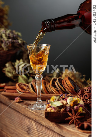 Herbal liquor is poured from a vintage bottle into a glass. Herbal liquor is poured from a vintage bottle into a glass. 142382402