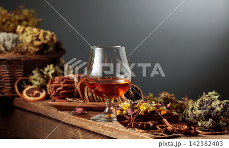 Herbal liquor and natural ingredients like herbs, roots, dried citrus slices, spices visible. 142382403