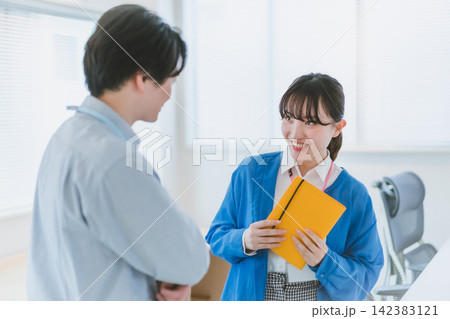 笑顔で同僚男性に話しかける手帳を持つ女性社員のオフィスラブ 笑顔で同僚男性に話しかける手帳を持つ女性社員のオフィスラブ 142383121