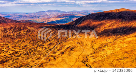 The photograph captures a vast expanse of mountains, illuminated by sunlight that creates stark contrasts between light and shadow. The photograph captures a vast expanse of mountains, illuminated by sunlight that creates stark contrasts between light and shadow. 142385396