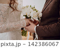 Tender close-up of groom holding bride s hands with a beautiful wedding bouquet between them, romantic wedding moment, love, connection and bridal celebration 142386067
