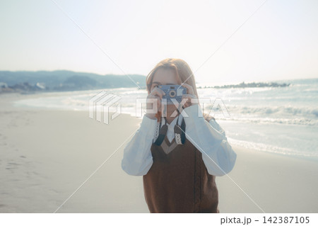 海辺でカメラを構えて写真を撮る20代女性 海辺でカメラを構えて写真を撮る20代女性 142387105