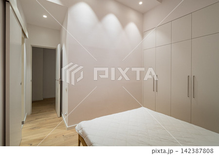 Minimalist modern bedroom with white bed, light wood flooring, builtin wardrobes, and soft recessed lighting in calm contemporary residential interior, with bedroom, minimalist, modern, white detail Minimalist modern bedroom with white bed, light wood flooring, builtin wardrobes, and soft recessed lighting in calm contemporary residential interior, with bedroom, minimalist, modern, white detail 142387808