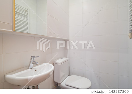 Bright modern bathroom with white toilet wall-mounted sink and mirrored cabinet in tiled interior 142387809